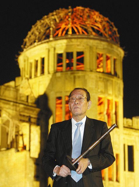 広島の原爆ドーム前で東京五輪聖火トーチを持つ坂井義則＝２００９年１０月