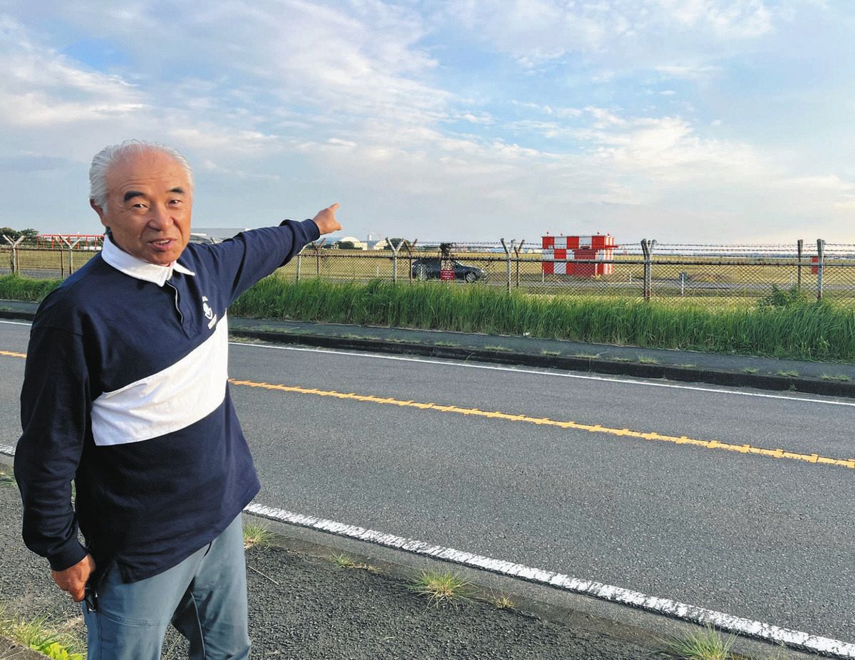 フェンスの先に広がる厚木基地を指差し、「艦載機移駐後も騒音はなくならない」と語る中坪清さん＝神奈川県大和市で