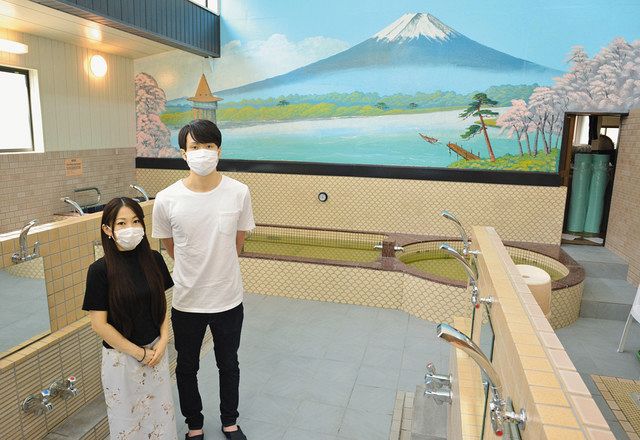 浴場に立つ４代目銭湯主の山田新太郎さん（右）、加奈さん夫妻。富士山のペンキ絵には、「矢切の渡し」など地域の風景も描かれている＝いずれも葛飾区金町で