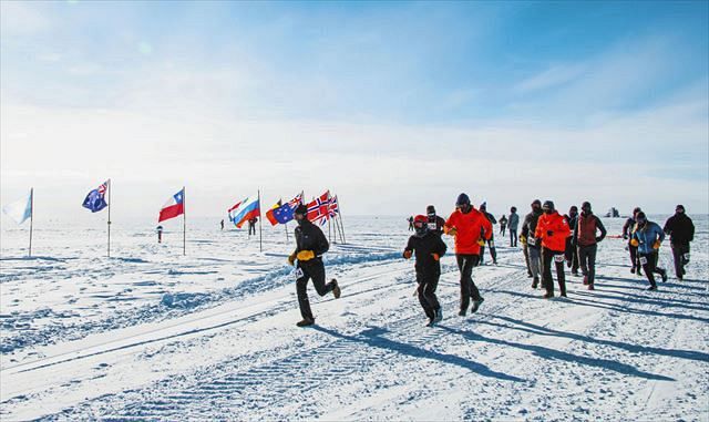 白夜に開かれたマラソン大会で、各国の国旗に囲まれた南極点の「セレモニアル・ポール」付近を走る研究者ら。真夏でも気温は氷点下２５度ほどだった＝１月