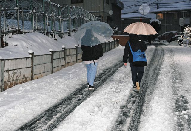 雪で轍の出来た住宅街の道を歩く人たち＝東京都八王子市で