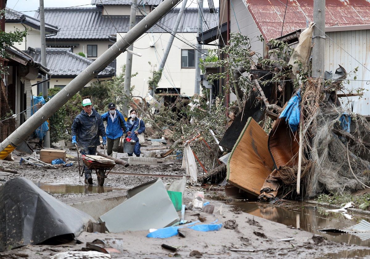 電柱が傾き泥の残る道を、一輪車で廃棄物を運ぶ人ら。この被害をもたらした台風19号は温暖化によって降水量が増えていたと分析された＝2019年10月15日、長野市で