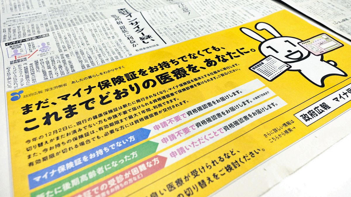 10月下旬、新聞に掲載された資格確認書についての政府広報。政府のマイナンバーPRキャラクター「マイナちゃん」が資格確認書とマイナンバーカードの2枚を持っている（由木直子撮影）