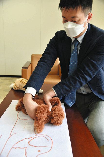 小型犬のぬいぐるみを使い、片手を背中、もう一方の手で心臓マッサージをする手法を説明する山本大樹さん＝名古屋市内で