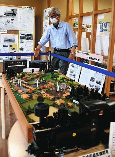小型蒸気機関車（手前）とガソリンカーの模型に挟んだジオラマ前で、企画展の説明をする岡野肇さん＝いずれも千葉県成田市で