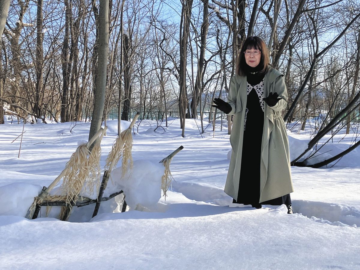 祭具「イナウ」の近くでアイヌ民族が受け継いできた文化について語る多原さん＝北海道大学内の遺跡保存庭園で