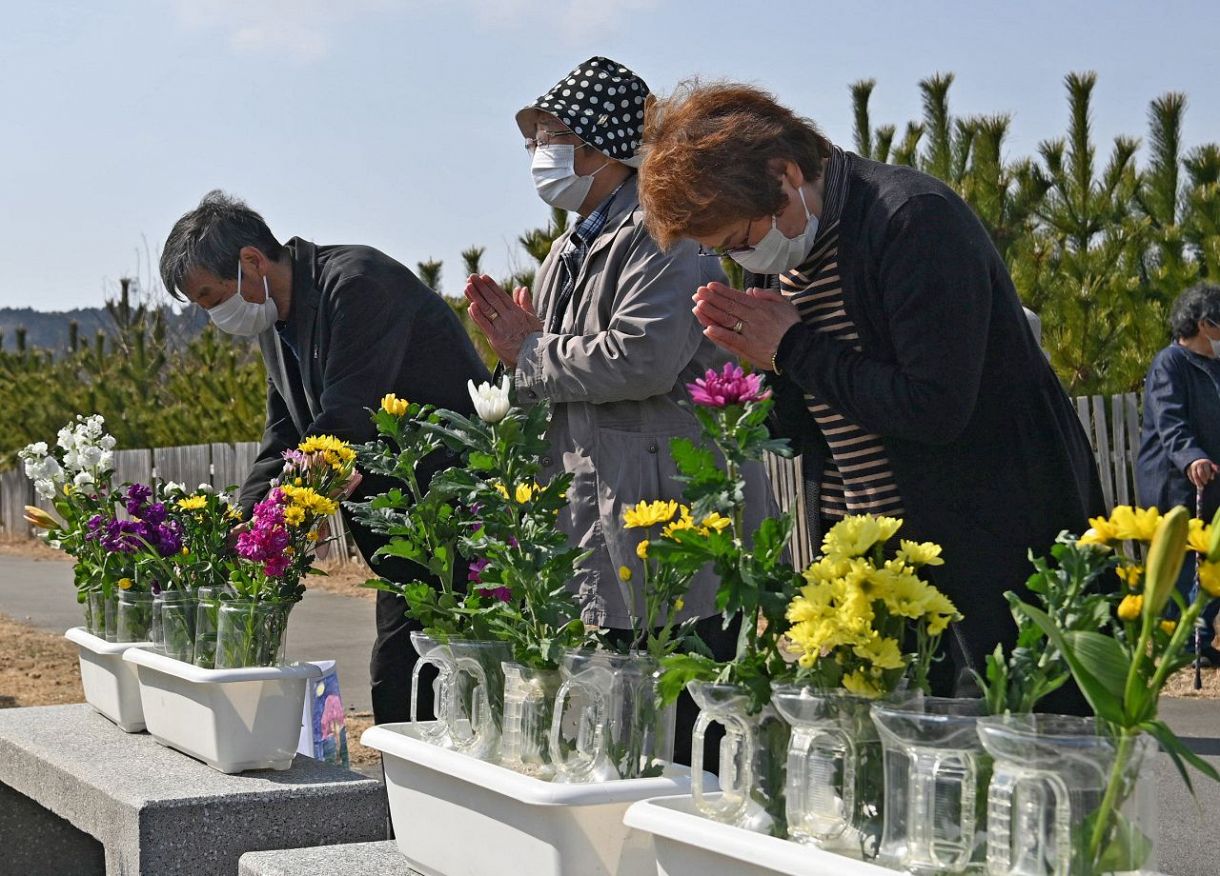 福島県いわき市久之浜防災緑地に設けられた献花台で手を合わせる田中千代さん（右）。「まだ見つからないいとことその息子に向けて手を合わせました」と話す＝２０２２年３月１１日（戸田泰雅撮影）