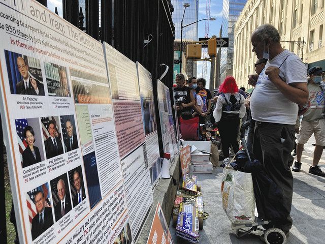 11日、米ニューヨークの世界貿易センタービル跡地の近くで、テロに関する陰謀論が書かれた看板を見る人＝杉藤貴浩撮影