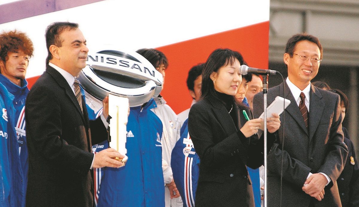 優勝報告セレモニーで、カルロス・ゴーン日産自動車社長（左）から優勝記念の「車」に関するエピソードを披露され、笑顔を見せる横浜Fマリノスの岡田武史監督＝2003年12月、横浜市西区のみなとみらいで