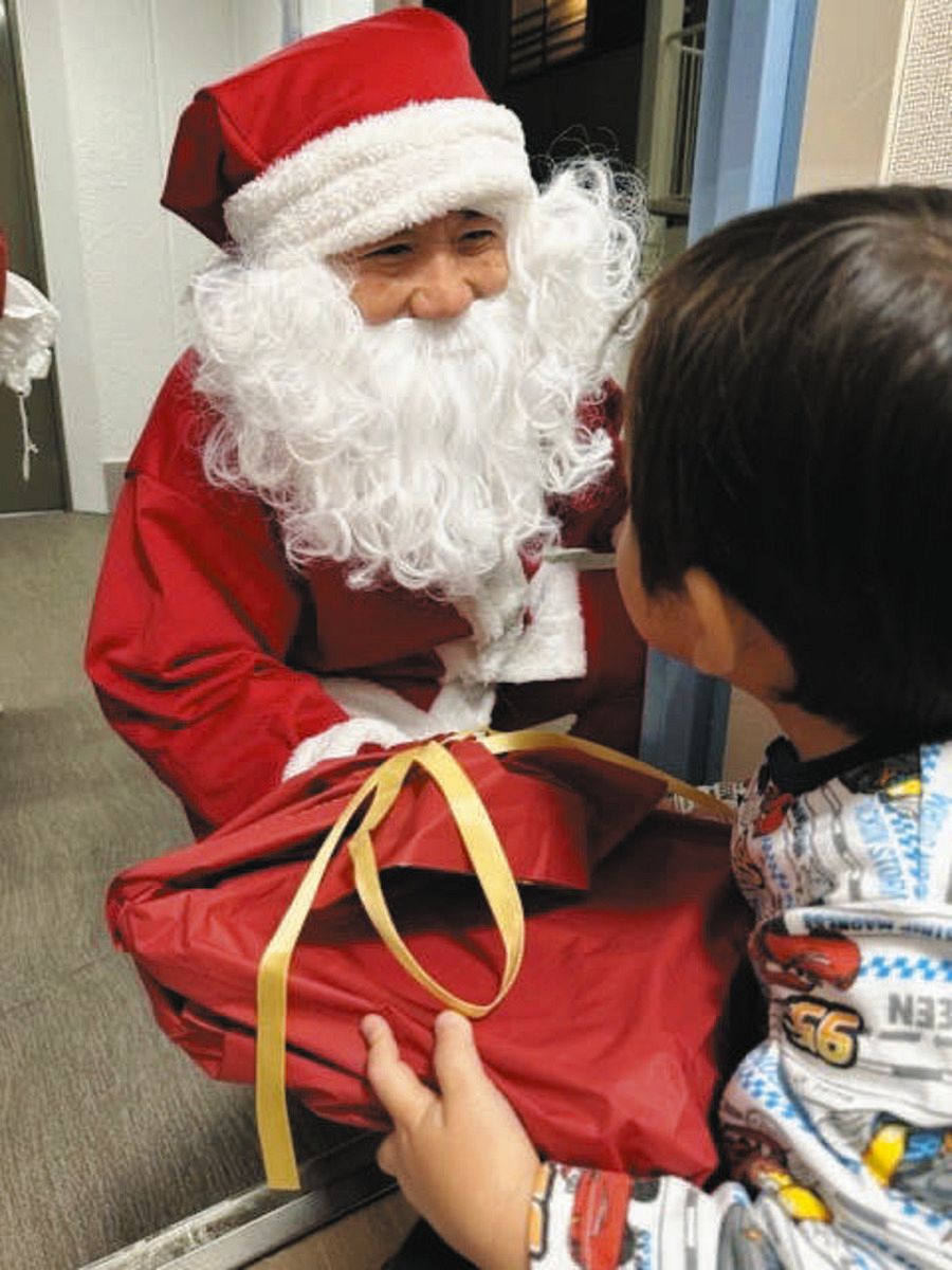 ボランティアのサンタ（左）からプレゼントを手渡される子ども＝昨年12月、NPO法人チャリティーサンタ提供）