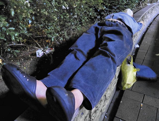 公園の花壇の縁で横たわり休む男性。手提げかばん一つで施設から逃げ出した＝東京都豊島区で