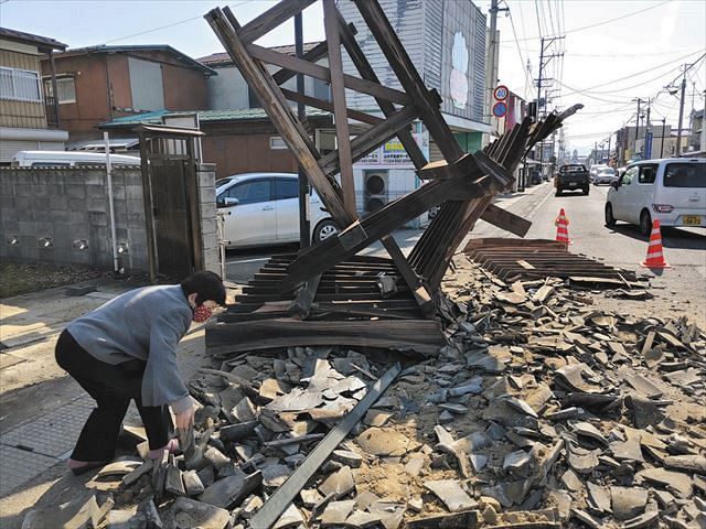 「１００年前からあった門扉が倒れてしまった」と話す粟野章さん。根こそぎ倒れ、瓦が飛び散っている＝福島県桑折町で
