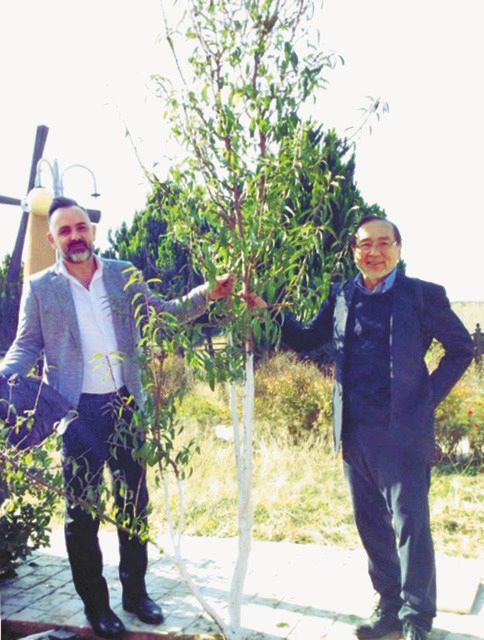 12月上旬、シリア西部ホムスで、12年前に自身が植えた桜の横で笑顔を見せる佐藤さん（右）とアラバッドさん＝佐藤さん提供