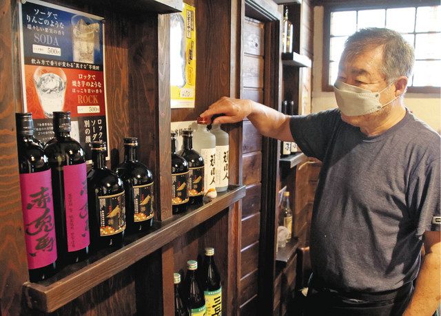 店内の酒瓶を整える野沢清司さん。今秋にも見込まれるアルコール類の値上げに戦々恐々という＝筑西市で
