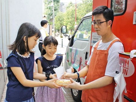 スタッフ（右端）から、ベーコンポテトドッグなどを受け取る女子児童＝文京区本駒込で