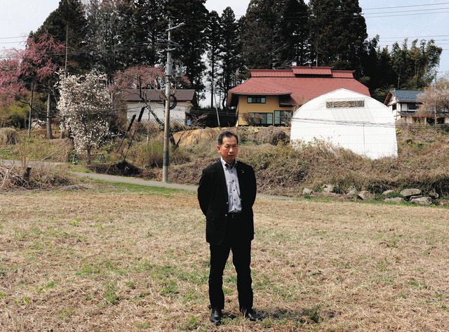 柱や梁を残し200年続く家（右奥の赤い屋根）を以前と同じように再建し、農地管理してきた土地に立つ紺野宏さん。