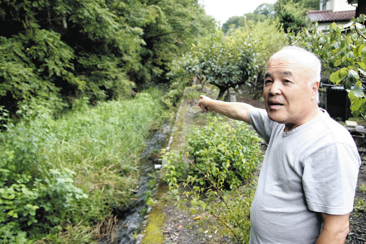 自宅脇の川沿いで、クマがいた場所を指さす須崎さん＝東京都あきる野市で