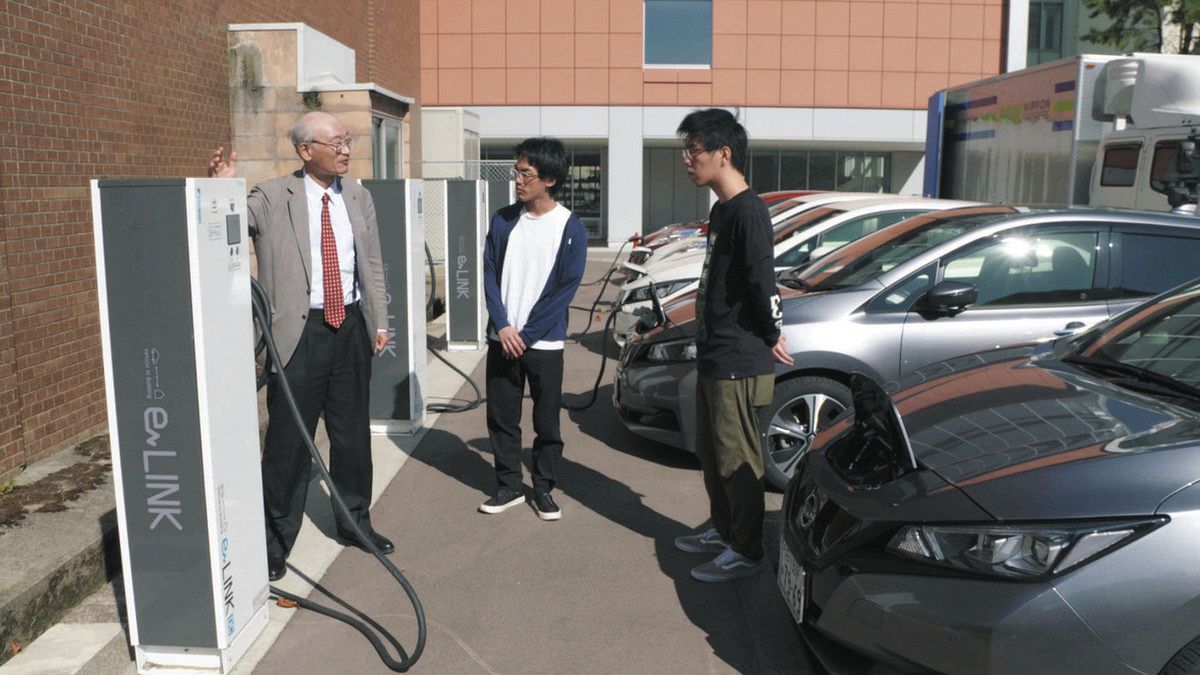 金沢工業大扇が丘キャンパスのEV充電器前で学生と話す泉井良夫教授（左）＝同大提供
