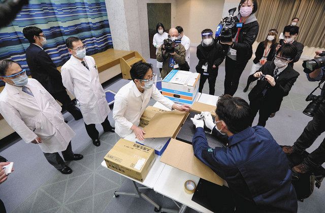 新型コロナウイルスのワクチン国内初接種を前に、搬入されたワクチンの箱を確認する病院関係者（左）＝１６日午後６時１９分、東京都内（代表撮影） 