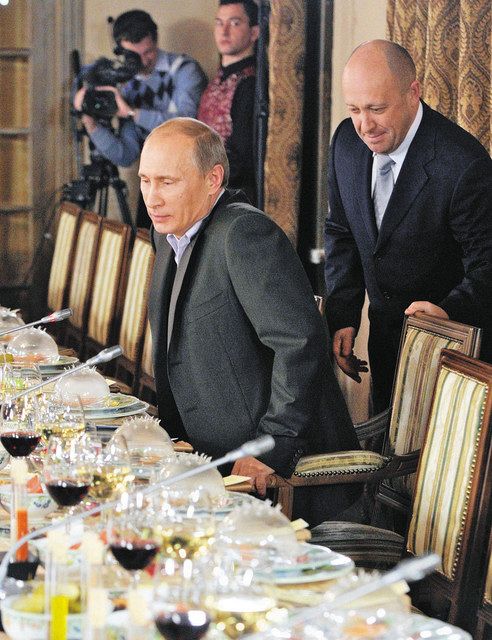２０１１年１１月、モスクワ州で、プーチン氏（左）の着席を助ける「プーチンのシェフ」プリゴジン氏＝ロシア紙コメルサント