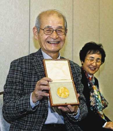 ノーベル賞の授賞式から帰国し、記者会見でメダルを披露する吉野彰・旭化成名誉フェロー。右は妻久美子さん＝１５日、成田空港で