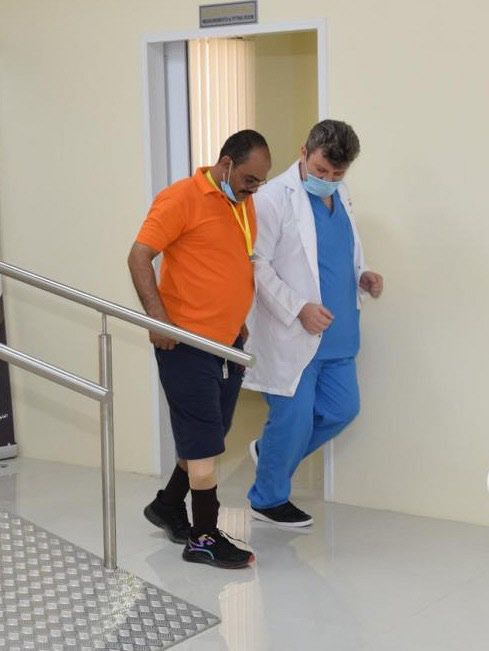 オマーン南部サラーラで11月上旬、新しい義足をつけた男性と歩行訓練をするオズゴルさん㊨＝アラブ義足センター提供