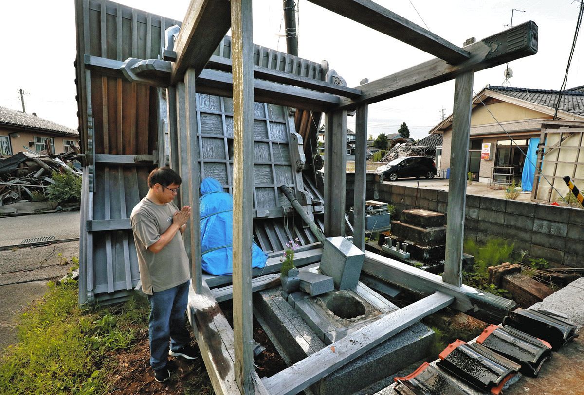 鐘突き堂が倒れて壊れた墓の前で手を合わせる寅口隆さん＝8日、石川県珠洲市正院町の徳勝寺で