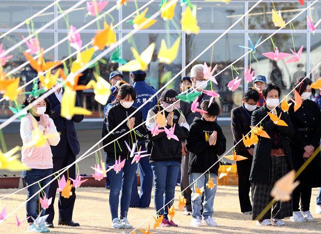 東日本大震災から１１年、折り鶴が飾られた広場で地震発生時刻に合わせて黙とうする人たち＝２０２２年３月１１、福島県大熊町（沢田将人撮影）