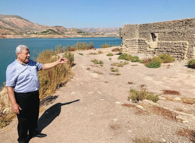 １０月、イラク北部ドホークのダム湖で、渇水で３７年ぶりに姿を現した建物を示すラマダン教授（蜘手美鶴撮影）