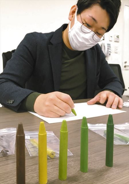 ５種類の茶を原料に使ったクレヨン。（左から）ほうじ茶、煎茶、かぶせ茶、玉露、抹茶）を紹介する前野安治さん＝滋賀県甲賀市役所で