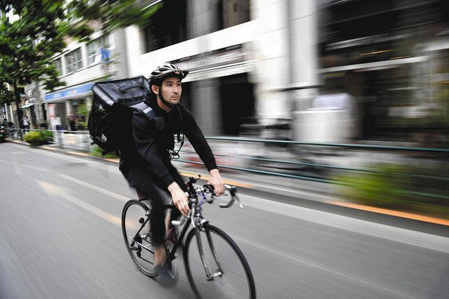「ウーバーイーツ」の黒い箱形リュックを背負い、街を疾走する三宅諒選手＝新宿区で