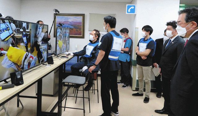 患者の処置室の映像情報を外の医師らがモニターで共有する実証実験を視察する福田市長（右から２人目）ら