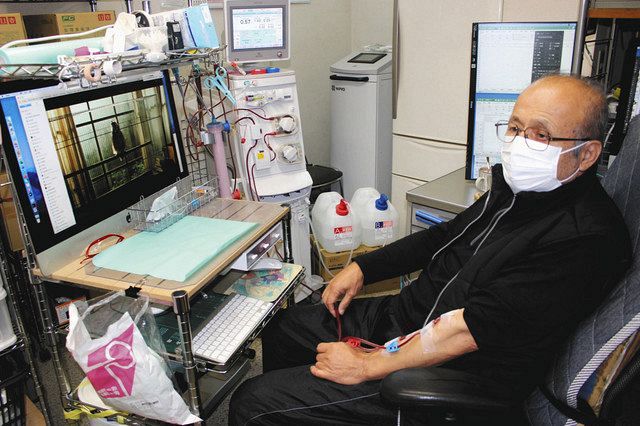 自宅で仕事机に向かいながら、自分で人工透析を行う長沼世紀さん＝東京都世田谷区で