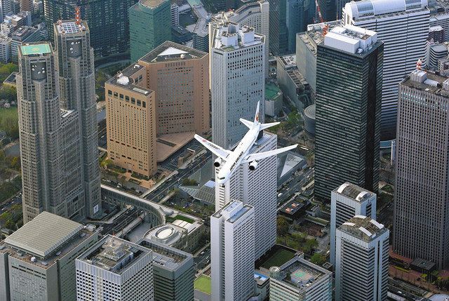 羽田空港への新ルートの運行が始まり、都心上空を飛ぶ旅客機。左は東京都庁＝４月３日、東京都内で、本社ヘリ「おおづる」から