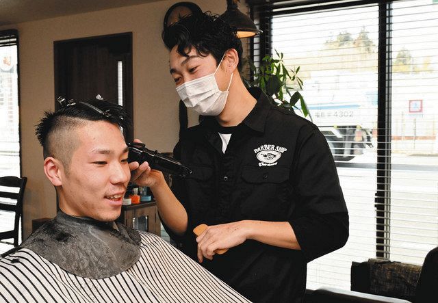 客と談笑しながら髪を刈る草野倫仁さん（右）＝福島県富岡町で