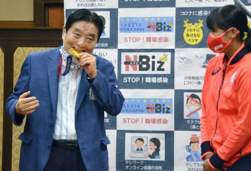 Nagoya Mayor Takashi Kawamura bites the gold medal of Tokyo Games Olympian Miu Goto, a member of the Japan softball team, at the Nagoya city hall in Aichi Prefecture on Aug. 4, 2021. (Kyodo)
