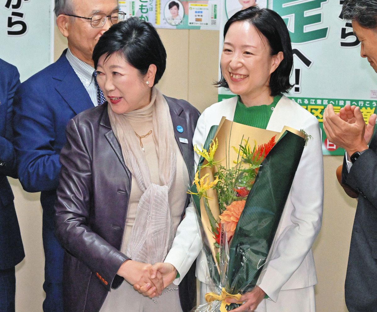 東京都江東区長選で当選し、駆けつけた小池都知事（左）と握手を交わす大久保さん。白のジャケットと緑の服やポスターは小池氏のイメージと重なる