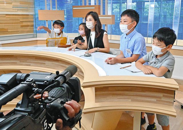 テレビ局のスタジオで森田美礼アナウンサー（左から３人目）からニュース原稿の読み方を学ぶ子どもたち＝千代田区で