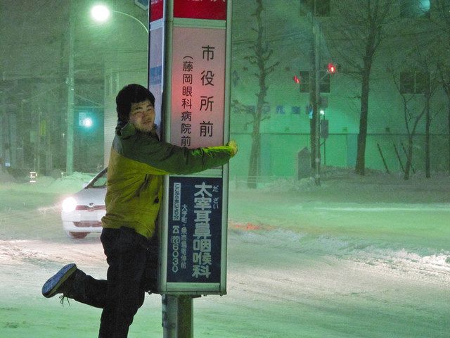 クリスマスイブの夜、見つけた喜びのあまりバス停に抱きつく飯島さん＝北海道函館市で 