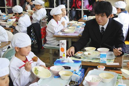 「茶葉入りつくね」を食べる子どもを笑顔で見守る太田響祐さん（右）＝いずれも富士市立田子浦小学校で