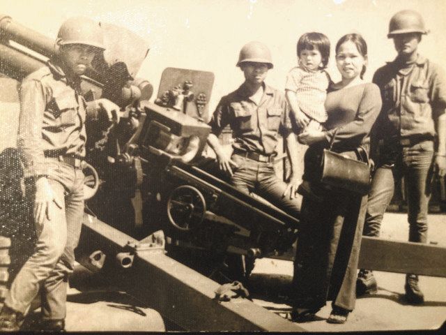 祖母に抱っこされる南雅和さん（右から３人目）。ベトナム共和国（南ベトナム）の軍人だった父の勤務地で兵士とともに撮影＝１９７１年１月１５日、南ベトナムで（本人提供）