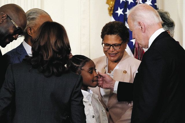 ２５日、米ホワイトハウスで大統領令に署名した後、ジョージ・フロイド氏の娘（中）のほほをなでるバイデン米大統領（右）＝ＡＰ 