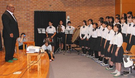 ナミビアの国歌を歌ってルスウェニョ大使（左）を歓迎する生徒たち＝町田市で