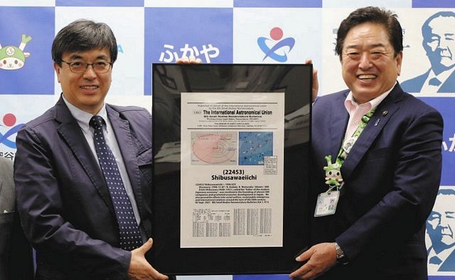 小惑星の「命名額」を手に笑顔の渡辺和郎さん（左）。右は小島進市長＝埼玉県深谷市役所で