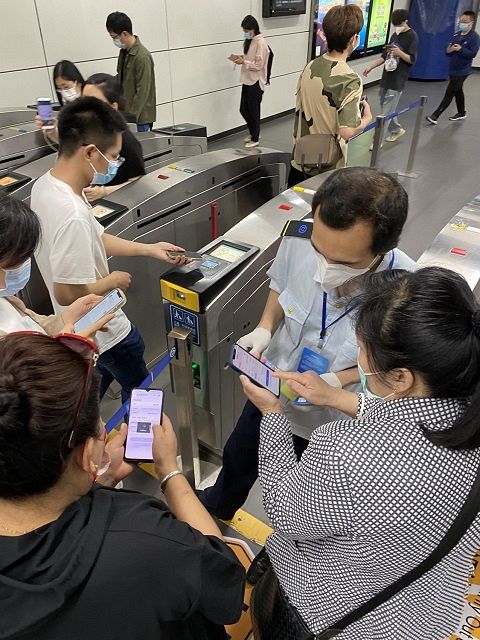 ﻿北京市内の地下鉄駅で9日、乗客のスマートフォンに表示された陰性証明を確認する駅職員（右奥）