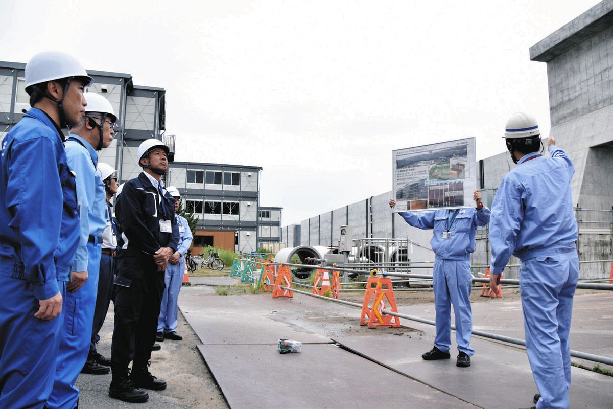 防潮堤（右側後方）建設工事の進捗状況について説明を聞く首長たち＝7月、茨城県東海村で