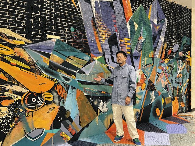 クリスタルなどを親子で描いた壁画の説明をする佐川さん
