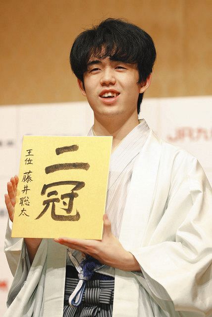 最年少で二冠を達成し、記者会見で色紙を手に笑顔の藤井聡太新王位＝、福岡市内のホテルで