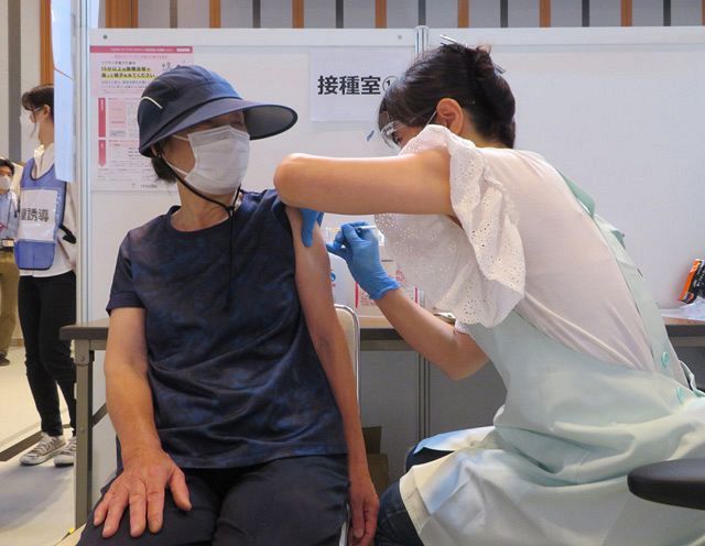 大規模接種会場で新型コロナウイルスワクチンの接種を受ける女性（左）