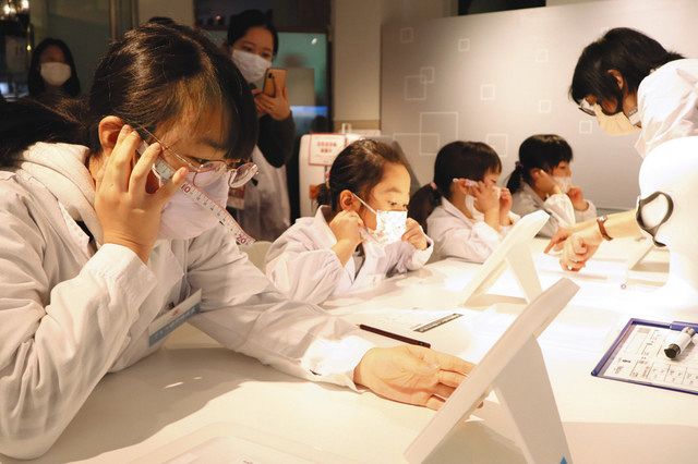鏡を見ながら口元の長さを計測し、適切なマスクの大きさを考える子どもたち＝東京都江東区のキッザニア東京で